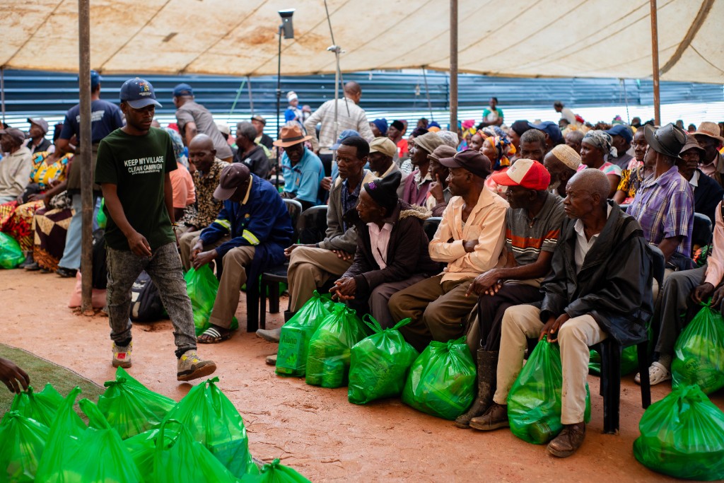 Elderly men seated with green Christmas hampers under the tent